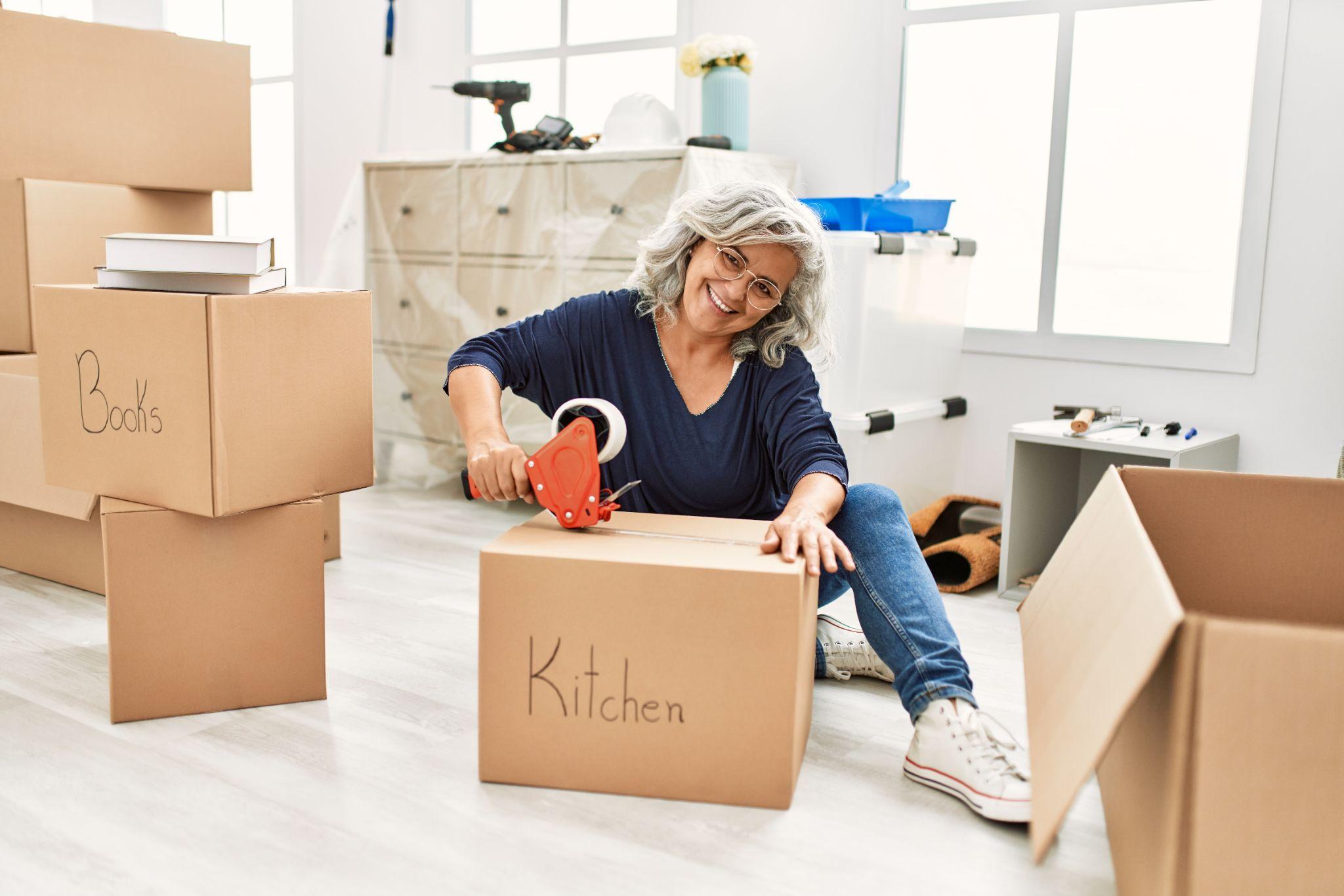 Lady sitting on floor taping up cardboard box labelled kitchen