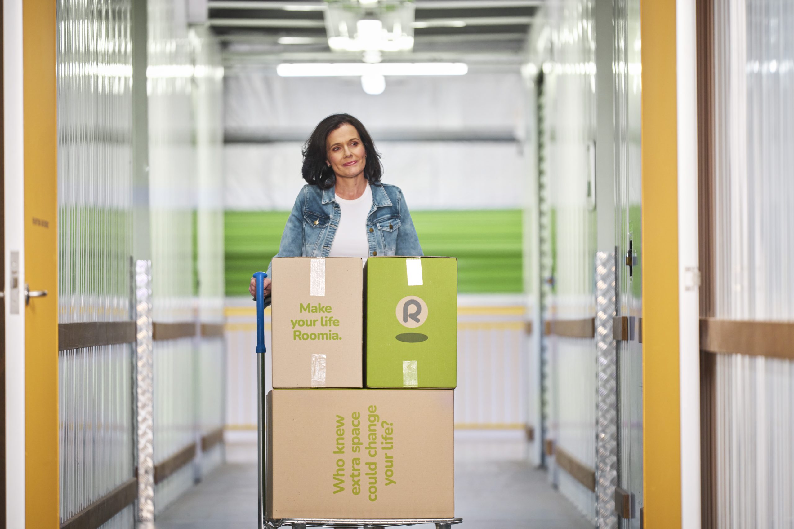Woman using complimentary trolley to move stacked boxes into an inside self storage unit.