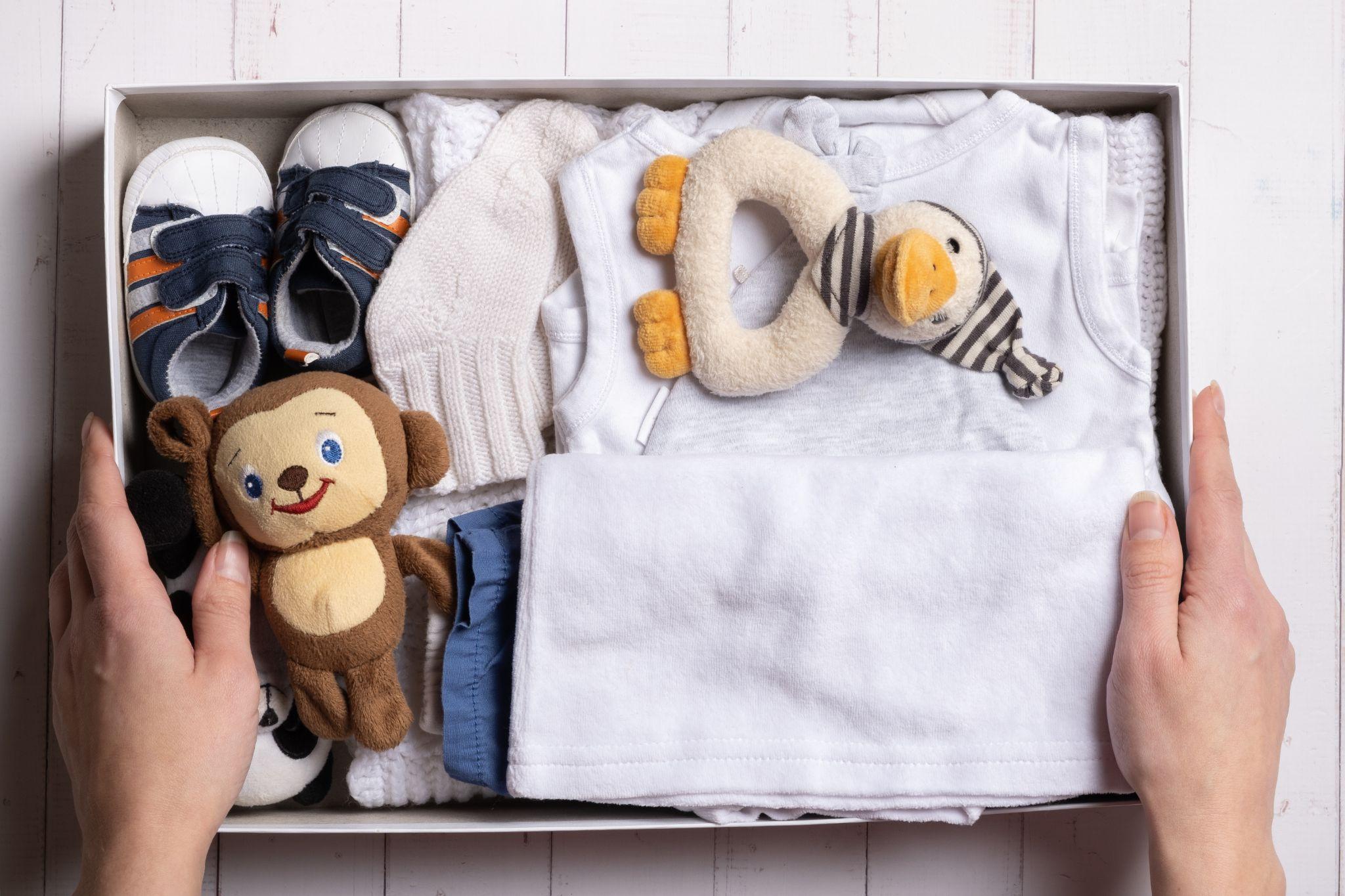 A packed cardboard box with baby clothes and teddy bear